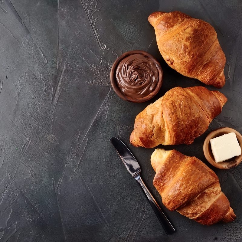 Sweet french croissant with chocolate cream and butter on black concrete tables.